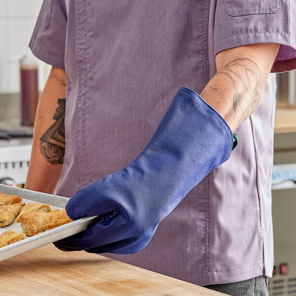 A person wearing a Tucker Safety blue oven mitt holding a tray of food.