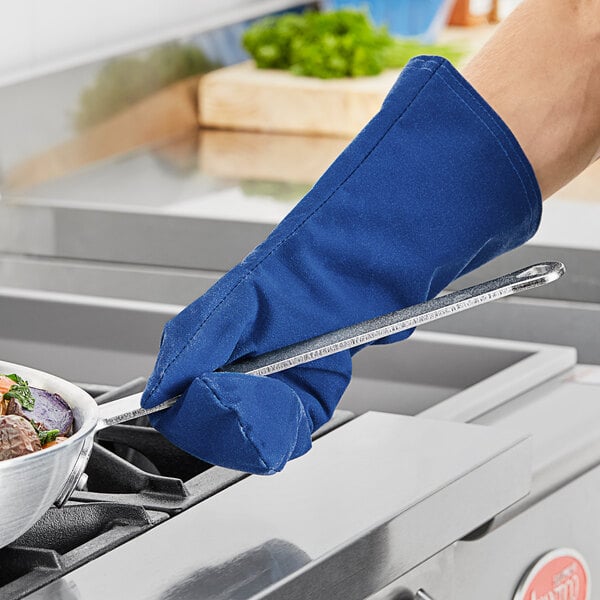 A person wearing a Tucker Safety blue oven mitt using a spatula to cook over a pan.