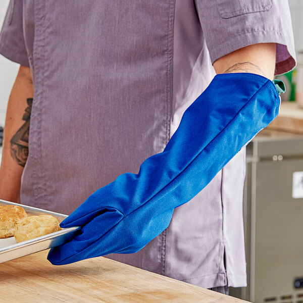 A person wearing a Tucker Safety blue Nomex oven mitt holding a tray of food.