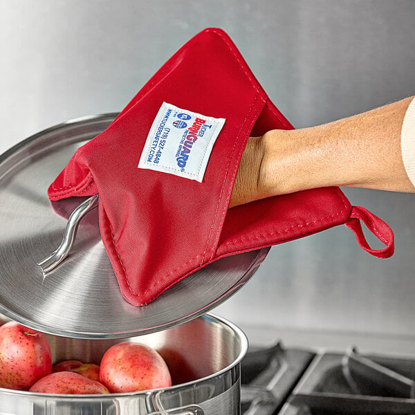 A hand using a Tucker Safety red poly-cotton hot pad to hold a pot over apples.