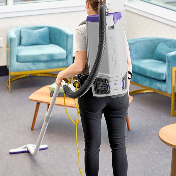 A woman using a ProTeam GoFit backpack vacuum cleaner to clean a room.