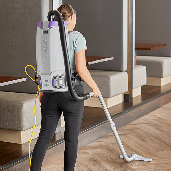 A woman using a ProTeam GoFit backpack vacuum in a professional kitchen.