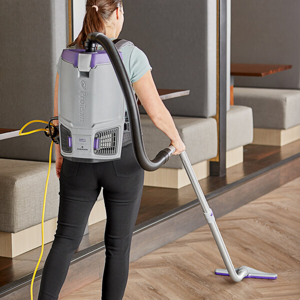 A woman using a ProTeam GoFit backpack vacuum to clean the floor.