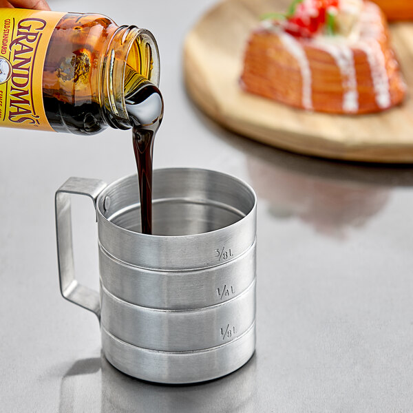A person pouring brown liquid into a metal measuring cup.