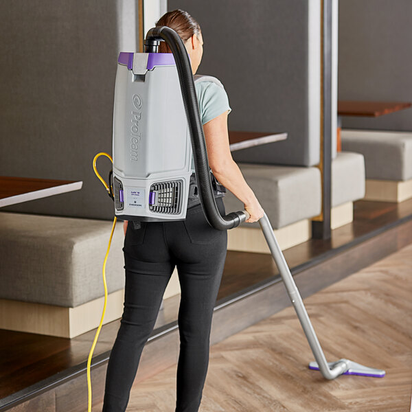 A woman using a ProTeam backpack vacuum to clean a restaurant kitchen.