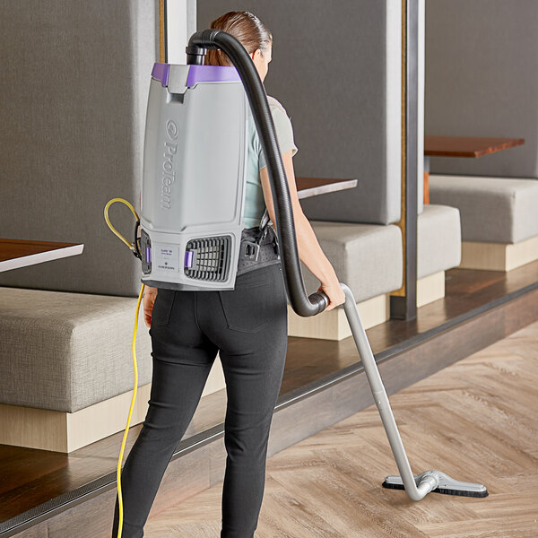 A woman using a ProTeam GoFit backpack vacuum in a professional kitchen.