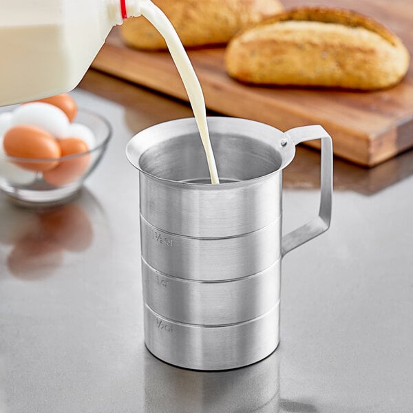 A person using a Choice aluminum measuring cup to pour milk.