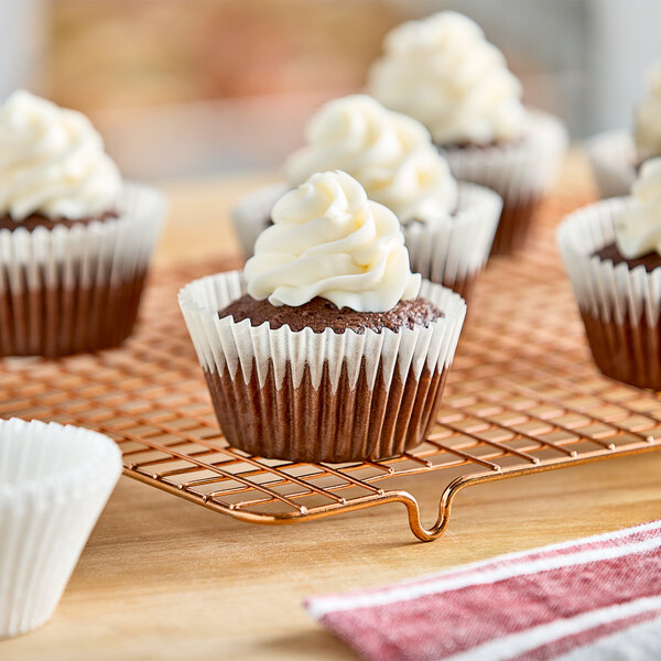 A group of 2 1/4" x 1 7/8" white fluted cupcakes with white frosting on a cooling rack.