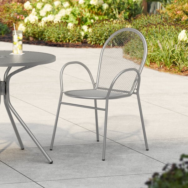 A Lancaster Table & Seating Harbor Gray Steel Mesh Outdoor Arm Chair on a patio.