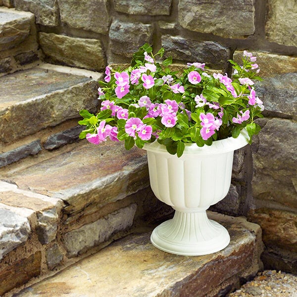 A Novelty Manufacturing Co. white urn planter with pink and purple flowers.