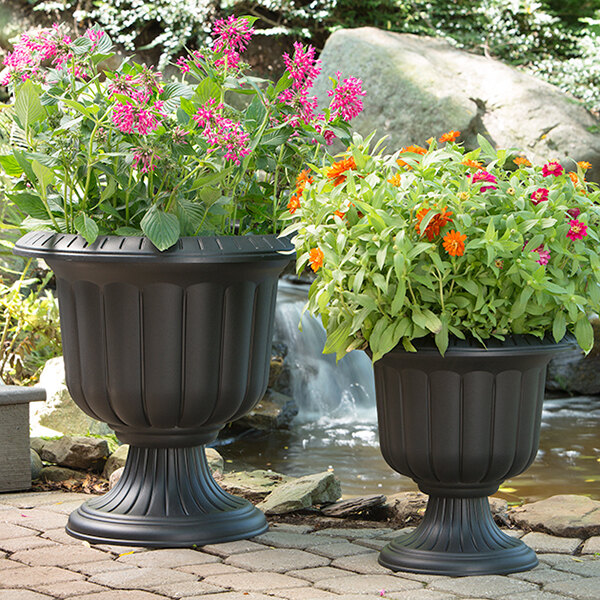 Two Novelty Manufacturing Co. black urn planters with flowers in them on an outdoor patio.