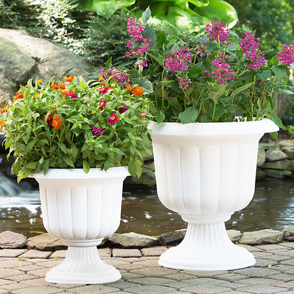 Two Novelty Manufacturing Co. white urn planters with flowers in them.