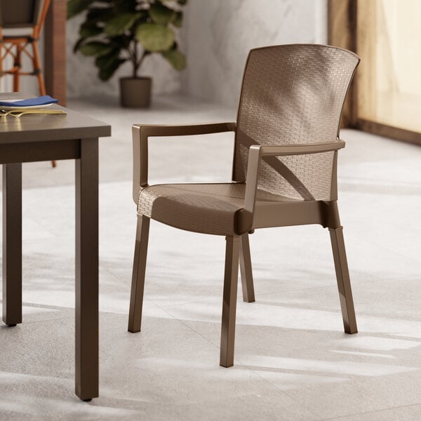 A brown Grosfillex Havana Classic stacking arm chair on an outdoor patio next to a table.