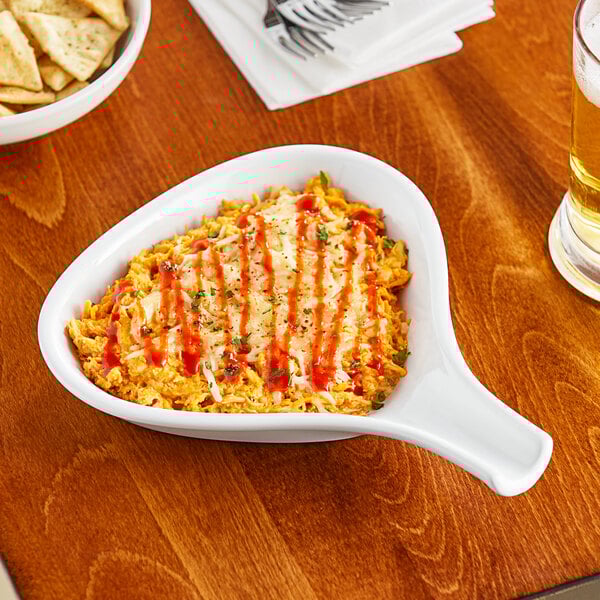 A white Acopa stoneware bowl filled with food on a table with chips and a glass of beer.