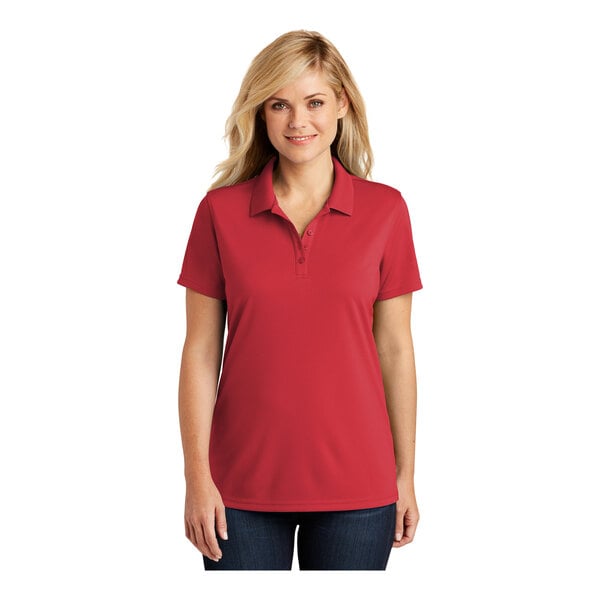 A woman wearing a rich red short sleeve Port Authority polo shirt with a collar.