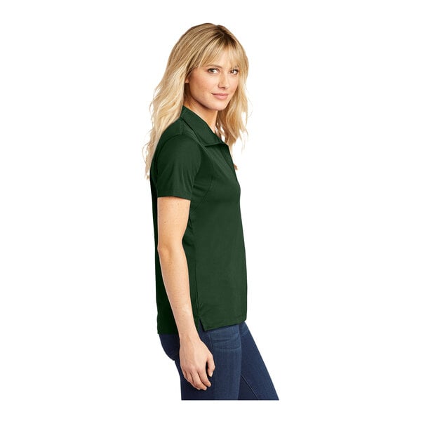 A woman wearing a Sport-Tek forest green short sleeve polo shirt.
