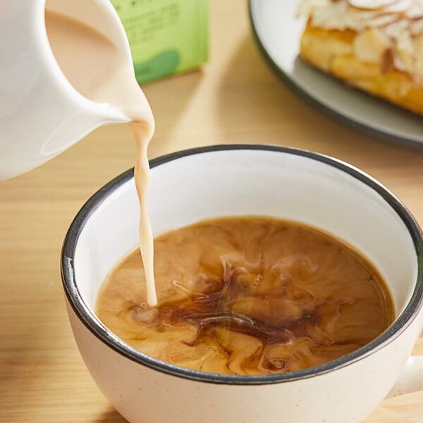 A cup of coffee with Tache Barista Pistachio Milk being poured into it.