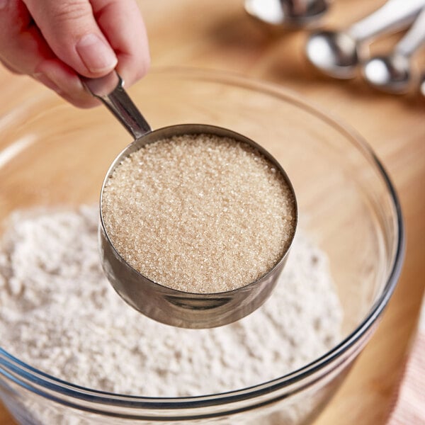 A person using a measuring spoon to measure Wholesome Sweeteners Organic Cane Sugar.