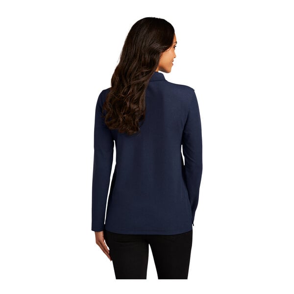 A woman wearing a medium navy blue Port Authority long sleeve polo with her hair pulled back.