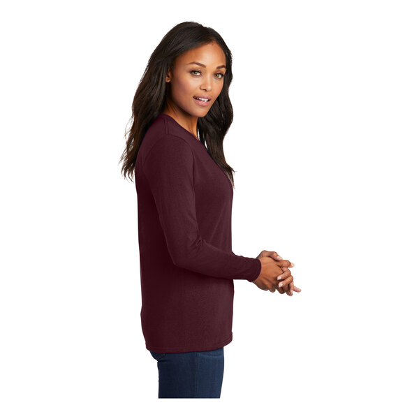 A woman wearing a maroon Port & Company long sleeve t-shirt.