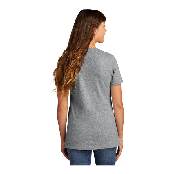 A woman with long brown hair wearing an athletic heather grey Port & Company t-shirt.
