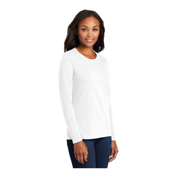 A woman wearing a white Port & Company long sleeve T-shirt.