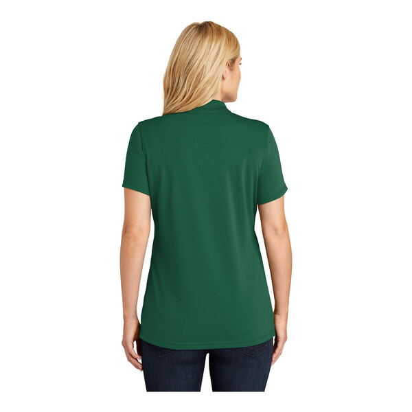 A woman wearing a deep forest green Port Authority short sleeve polo shirt.
