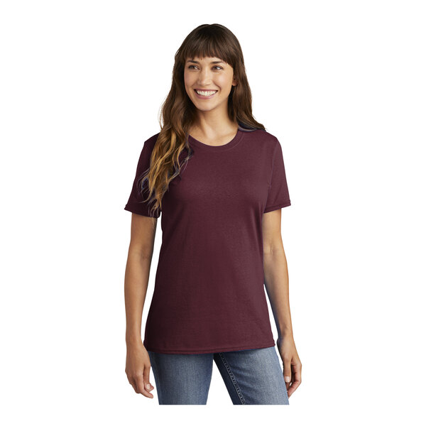 A woman wearing a Port & Company maroon short sleeve t-shirt.
