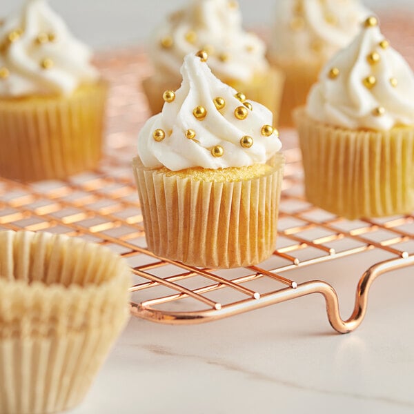 A Baker's Lane fluted Kraft mini cupcake wrapper with a cupcake with white frosting and gold beads.