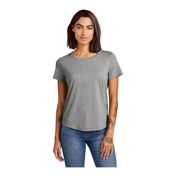 A woman with tattoos on her arms wearing a grey AllMade customizable tri-blend T-shirt.