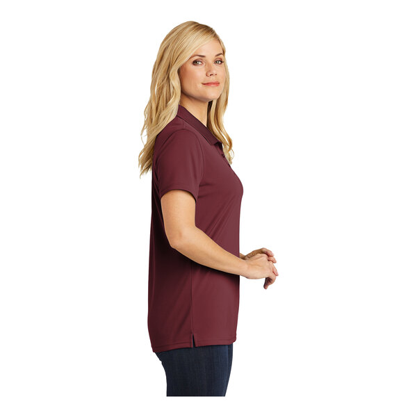 A woman wearing a burgundy Port Authority Dry Zone polo shirt.