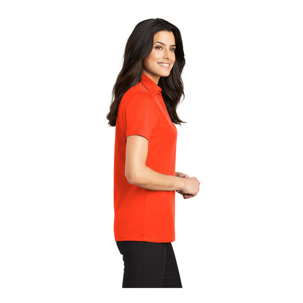 A woman wearing a Port Authority women's neon orange polo shirt.