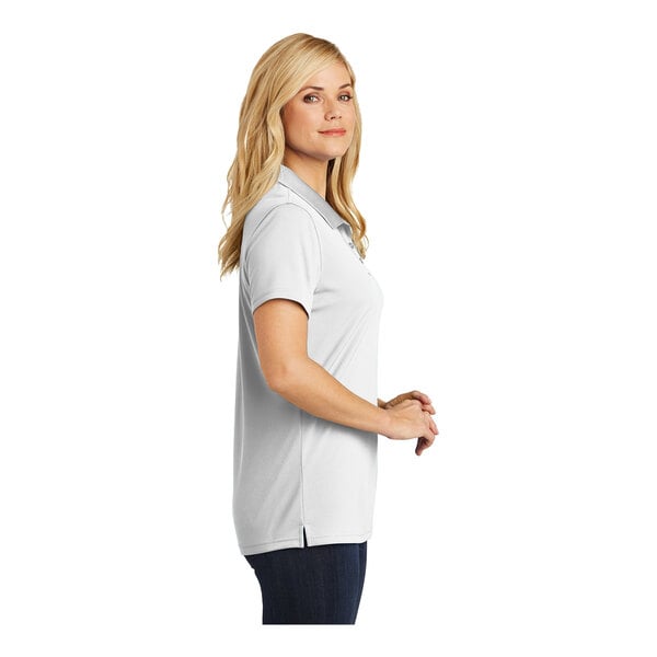 A woman wearing a white Port Authority Dry Zone polo shirt.