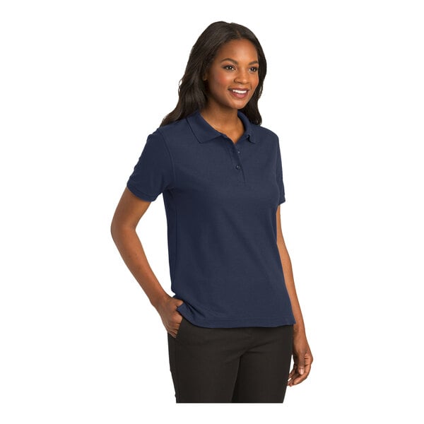 A woman wearing a navy Port Authority silk touch pique polo shirt.