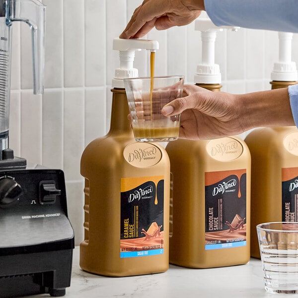 A large 64 fl. oz. bottle of DaVinci Gourmet Sugar-Free Caramel Flavoring Sauce with a pump dispenser being used to pour sauce into a glass.