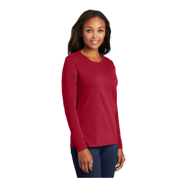 A woman wearing a red Port & Company long sleeve T-shirt.