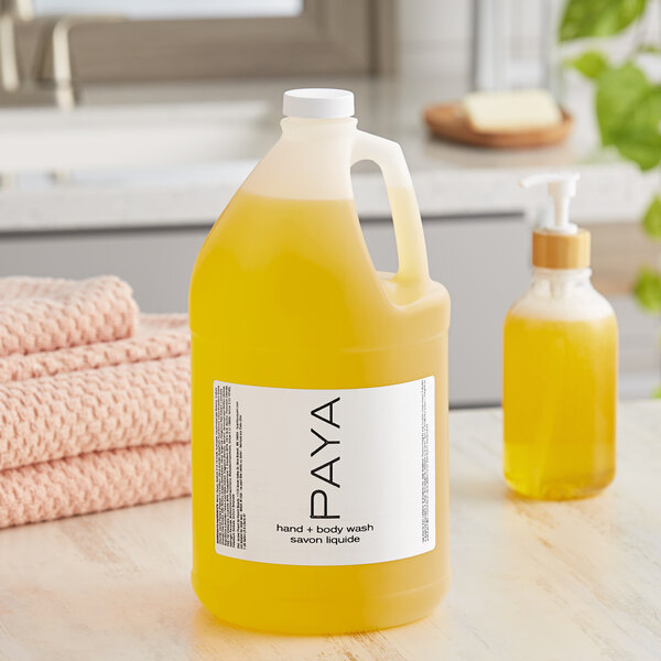 A yellow jug of PAYA Papaya liquid soap on a counter next to a bottle of liquid soap.