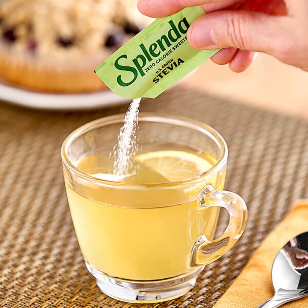 A hand pouring Splenda stevia into a glass of tea.