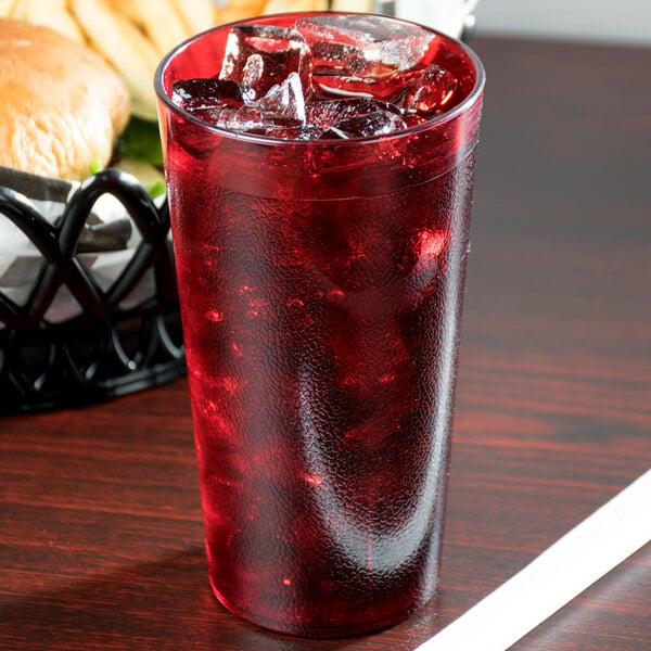 A Cambro ruby red plastic tumbler filled with red liquid and ice on a table with a burger.