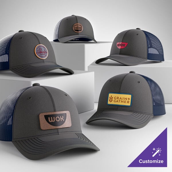 A collection of customizable grey and navy 6-panel trucker caps with mesh backs and various logo patches on the front.