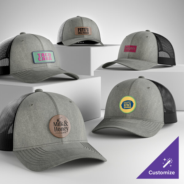 A collection of customizable heather grey and black 6-panel trucker caps with mesh backs and various logo patches on the front.