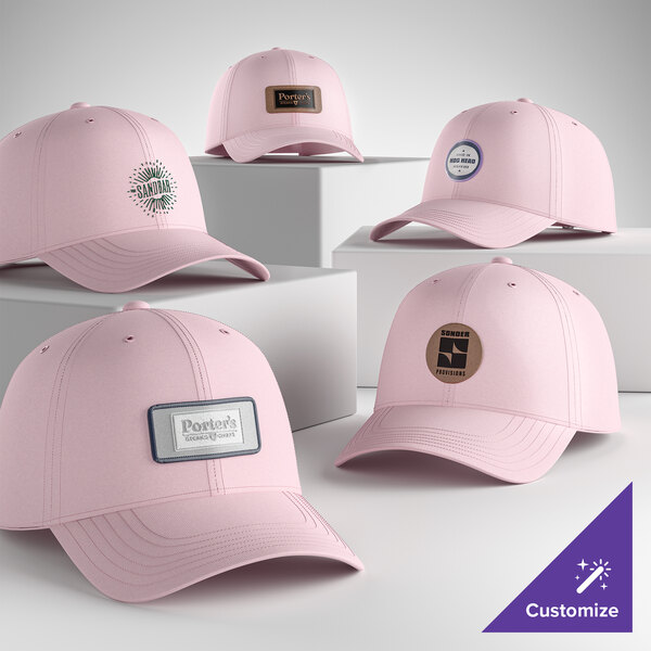A collection of light pink, customizable 6-panel dad caps with various logo patches displayed on white platforms.