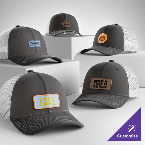 A collection of customizable grey and white 6-panel trucker caps with mesh backs and various branded patches on the front.