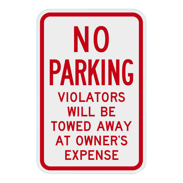 A white rectangular sign with red text that says "No Parking / Violators Will Be Towed Away At Owner's Expense" on it.