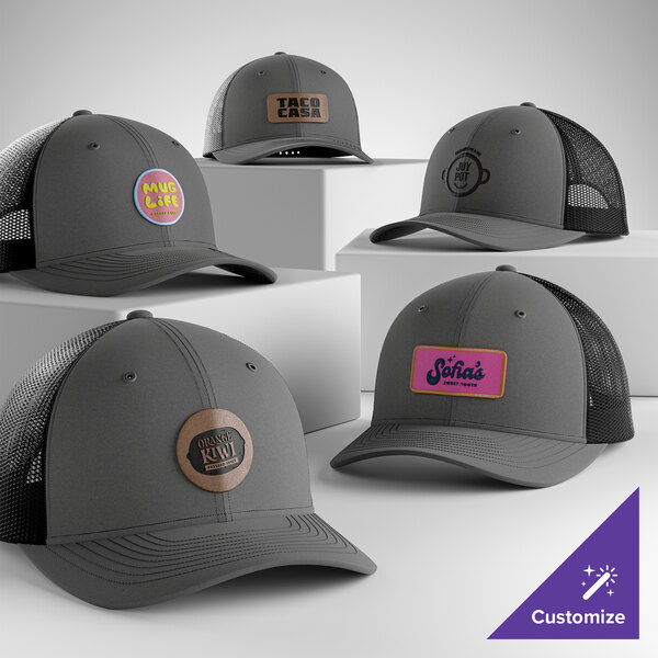 A collection of customizable graphite and black 6-panel trucker caps with mesh backs, each featuring different logo patches on the front.