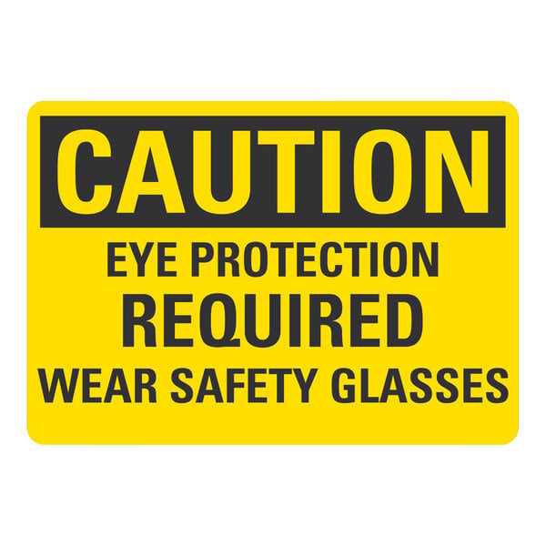 A yellow and black rectangular safety label with white text that says "Caution Eye Protection Required Wear Safety Glasses"