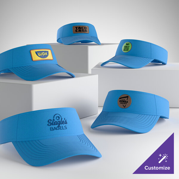 A collection of blue Port & Company CP45 customizable sapphire visors displayed on white blocks, each featuring different custom logos.