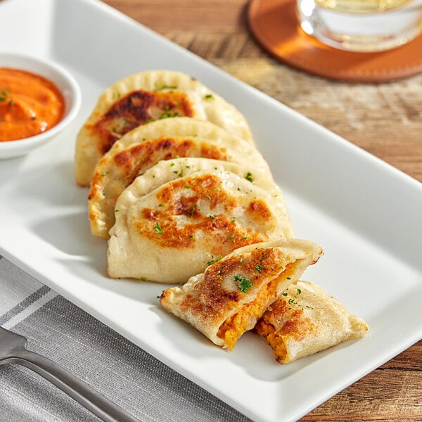 A plate of Jaju sweet potato and caramelized onion pierogies with cheese and sauce.