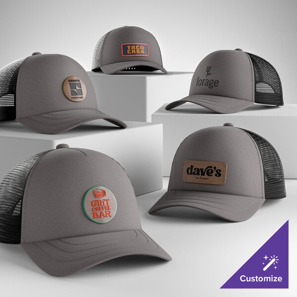 A group of customizable charcoal and black 5-panel foam trucker caps with mesh backs, each featuring different logo designs on the front.