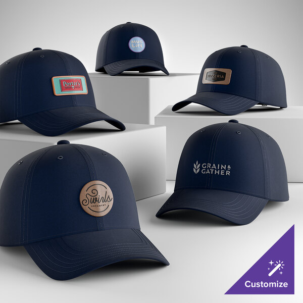 A collection of customizable navy blue 6-panel dad caps with various logo designs displayed on white platforms.